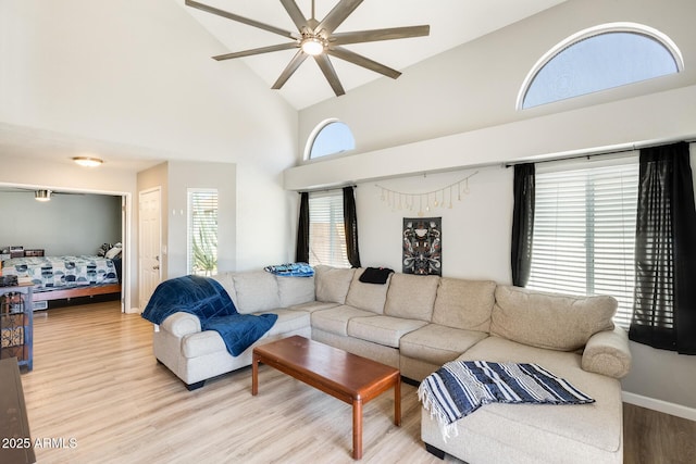 living room with ceiling fan, baseboards, high vaulted ceiling, and light wood-type flooring