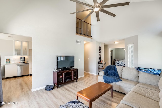 living area with a towering ceiling, ceiling fan, baseboards, light wood-type flooring, and visible vents