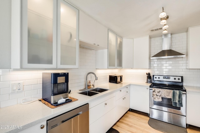 kitchen with visible vents, a sink, light countertops, stainless steel appliances, and wall chimney exhaust hood