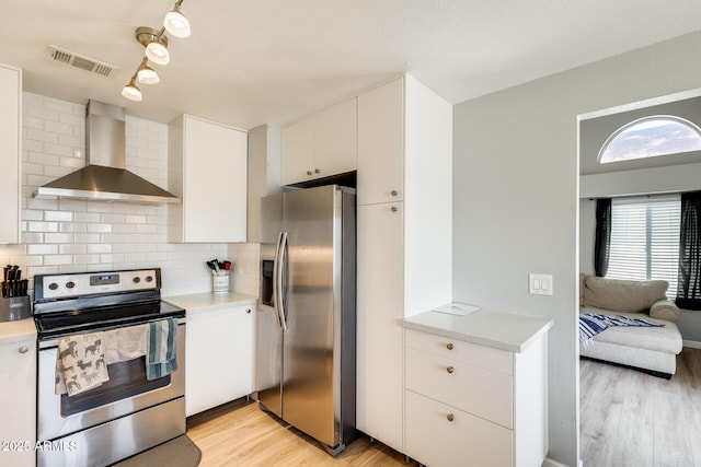 kitchen featuring visible vents, wall chimney range hood, light wood-type flooring, light countertops, and appliances with stainless steel finishes