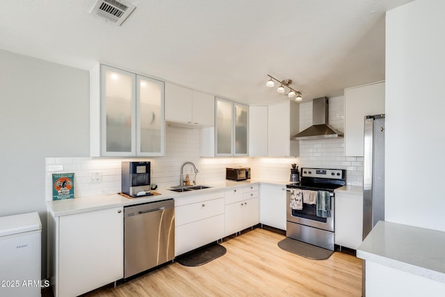 kitchen with visible vents, wall chimney exhaust hood, a sink, appliances with stainless steel finishes, and backsplash