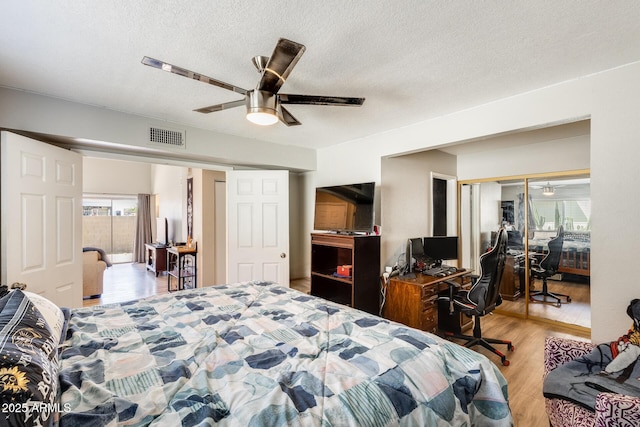 bedroom with ceiling fan, a textured ceiling, visible vents, and wood finished floors