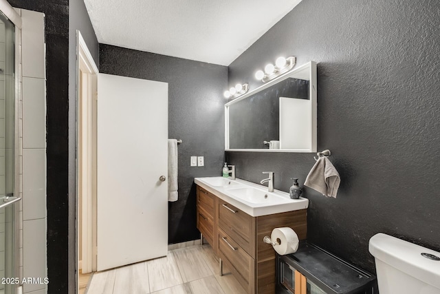 full bathroom with a sink, a textured wall, toilet, and double vanity