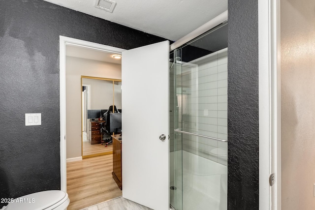 bathroom featuring a textured wall, a shower stall, toilet, and visible vents