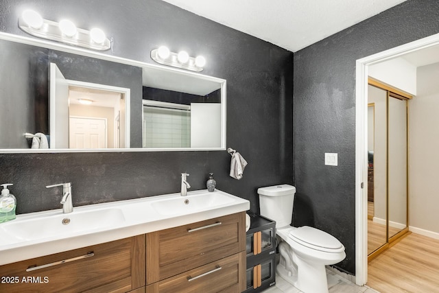 bathroom featuring double vanity, toilet, a sink, and wood finished floors