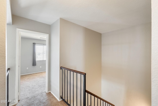 corridor featuring carpet floors, baseboards, and an upstairs landing