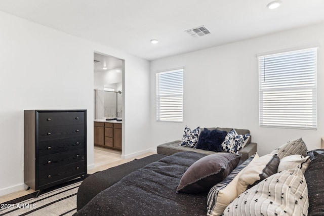 bedroom with baseboards, visible vents, ensuite bathroom, and light carpet