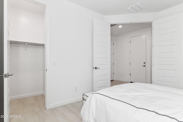 bedroom with baseboards, light wood finished floors, visible vents, a closet, and a walk in closet