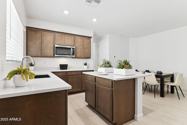 kitchen with visible vents, a sink, stainless steel microwave, a center island, and light countertops