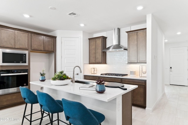 kitchen featuring visible vents, a sink, tasteful backsplash, stainless steel appliances, and wall chimney exhaust hood