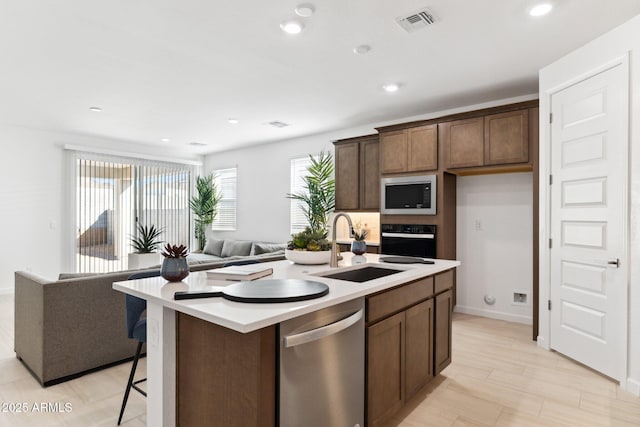 kitchen featuring black oven, built in microwave, open floor plan, stainless steel dishwasher, and a sink