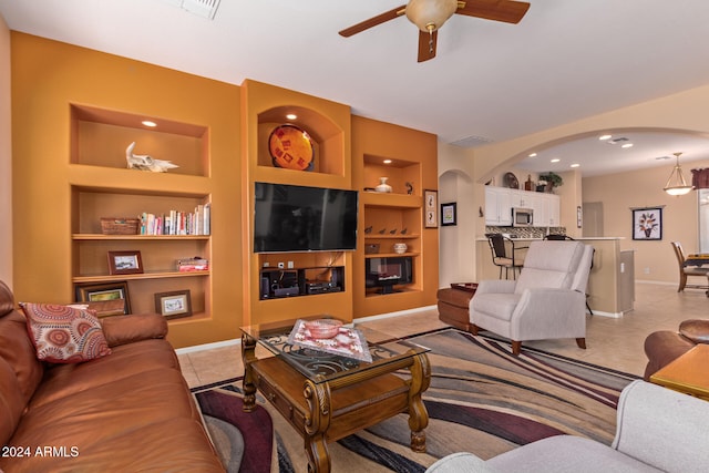 tiled living room with ceiling fan and built in shelves