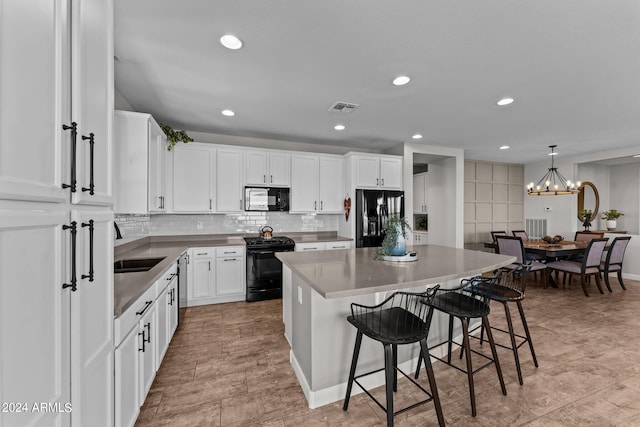 kitchen with a chandelier, a center island, white cabinetry, black appliances, and decorative light fixtures