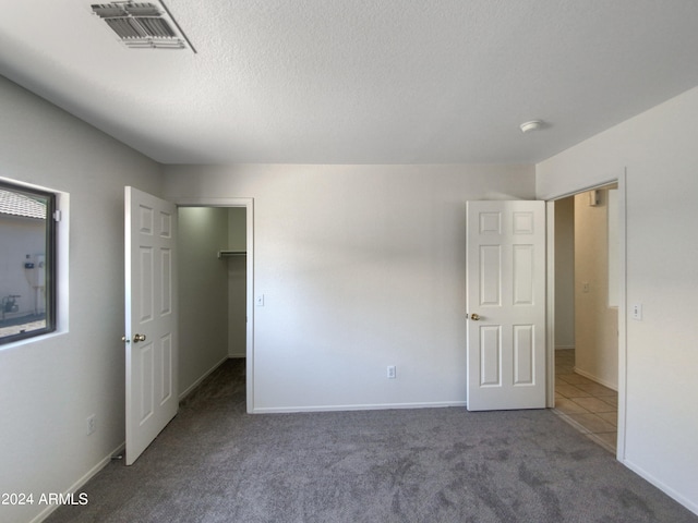 unfurnished bedroom featuring a walk in closet, a closet, dark colored carpet, and a textured ceiling