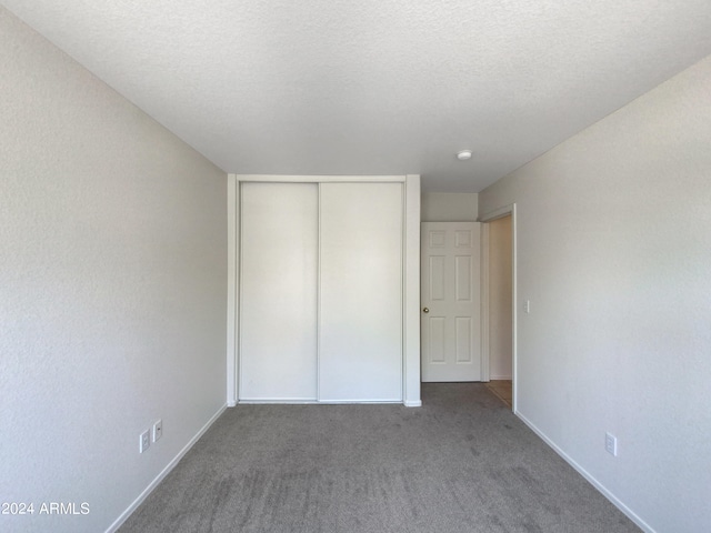 unfurnished bedroom featuring a textured ceiling, a closet, and dark colored carpet