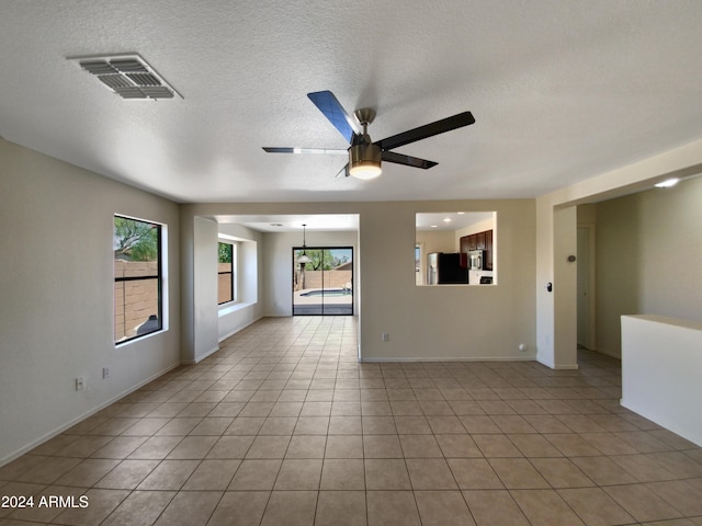 empty room with a textured ceiling, ceiling fan, and light tile flooring