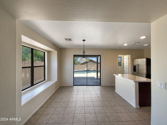 kitchen featuring stainless steel refrigerator with ice dispenser, light tile flooring, a textured ceiling, and decorative light fixtures