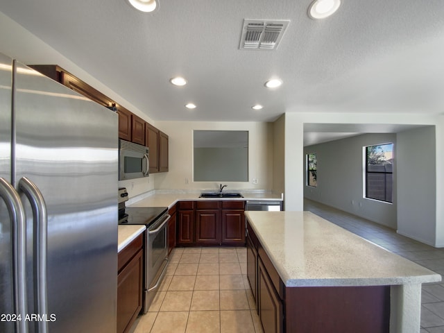 kitchen with a textured ceiling, a kitchen island, light tile floors, sink, and appliances with stainless steel finishes