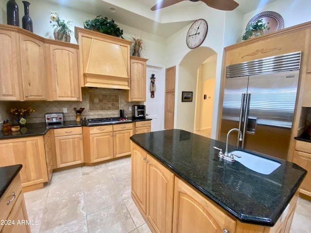 kitchen featuring backsplash, dark stone counters, stainless steel appliances, sink, and an island with sink