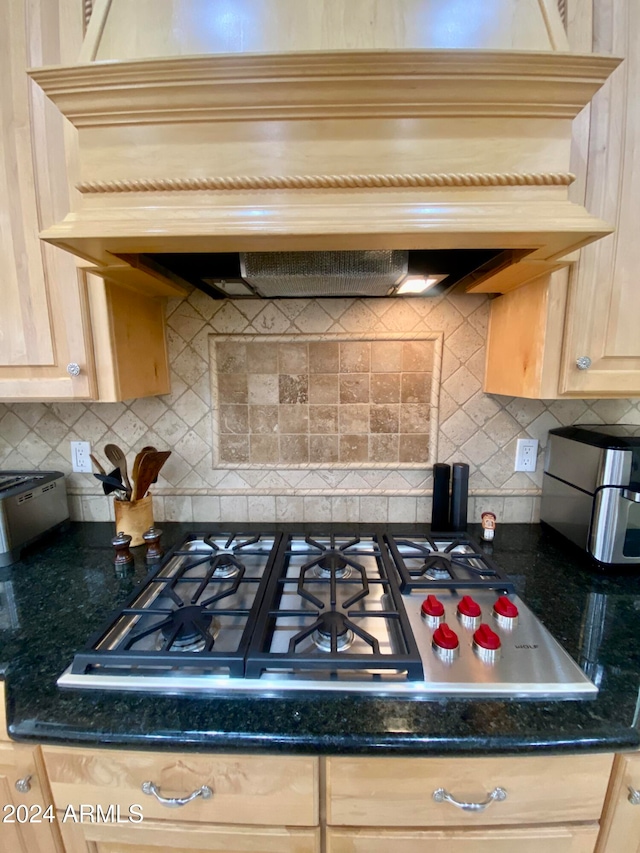 kitchen with dark stone countertops, light brown cabinetry, backsplash, and stainless steel gas cooktop