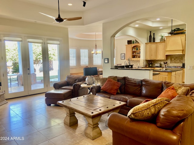 tiled living room with ceiling fan with notable chandelier, french doors, and a tray ceiling