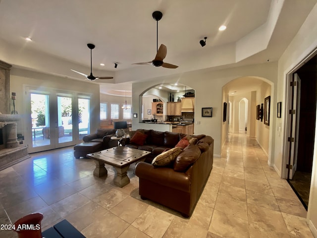 tiled living room featuring a raised ceiling, french doors, and ceiling fan with notable chandelier