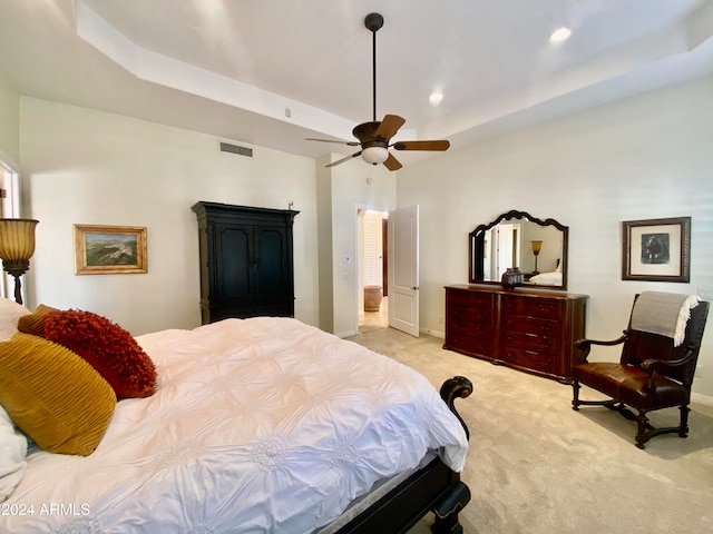 bedroom with light colored carpet, ceiling fan, and a tray ceiling