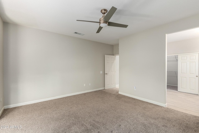 unfurnished bedroom featuring a closet, light carpet, a walk in closet, and ceiling fan