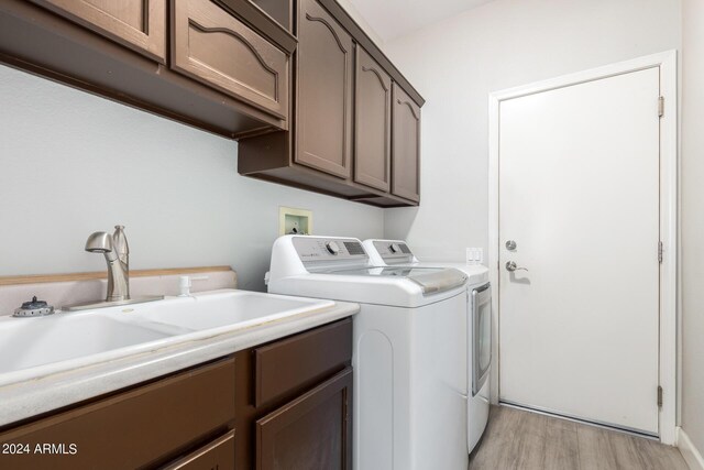 laundry area with sink, light wood-type flooring, independent washer and dryer, and cabinets