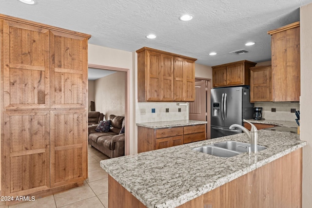 kitchen with light tile patterned flooring, stainless steel fridge, sink, backsplash, and light stone countertops