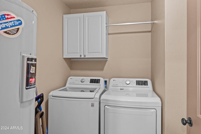 clothes washing area with cabinets, water heater, a textured ceiling, and separate washer and dryer