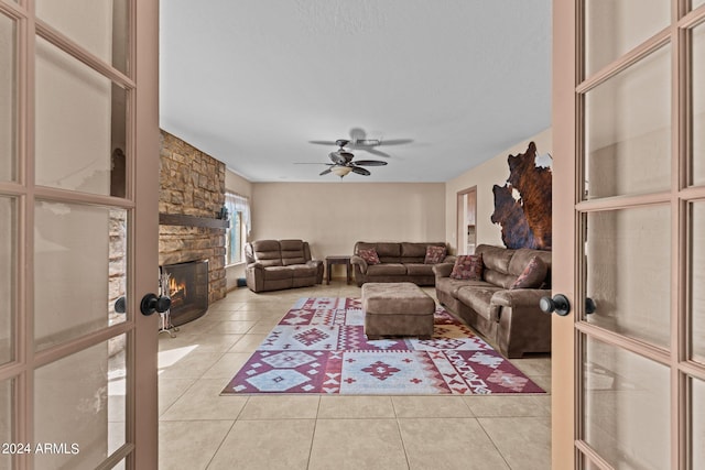 tiled living room featuring a stone fireplace, ceiling fan, and french doors