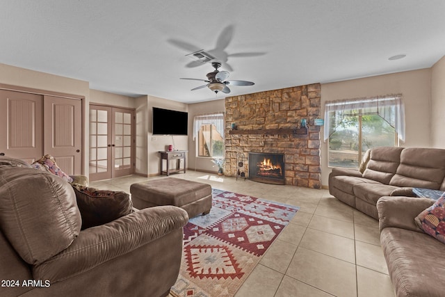 living room featuring light tile patterned floors, ceiling fan, french doors, and a stone fireplace