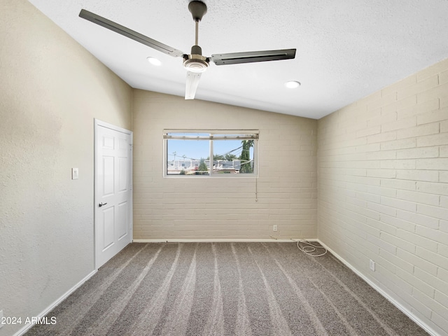 carpeted empty room featuring a textured ceiling, vaulted ceiling, and brick wall