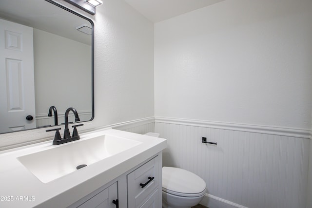 bathroom with toilet, a wainscoted wall, and vanity