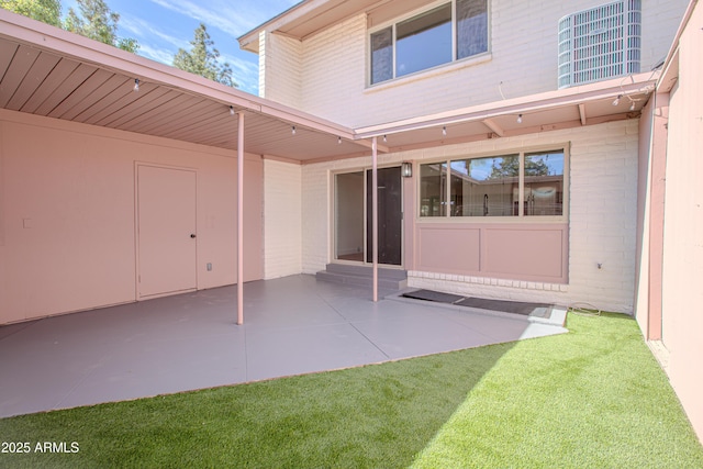 property entrance with brick siding, a patio, and a lawn