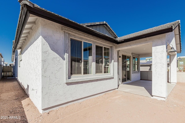 view of property exterior featuring board and batten siding, a patio area, fence, and stucco siding