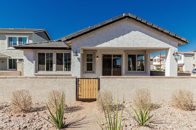 exterior space with a fenced front yard, a gate, a tile roof, and stucco siding