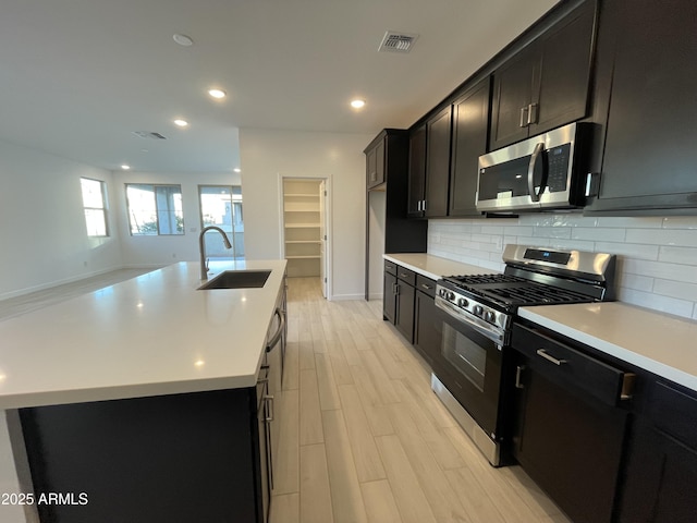 kitchen with stainless steel appliances, backsplash, a sink, and dark cabinets