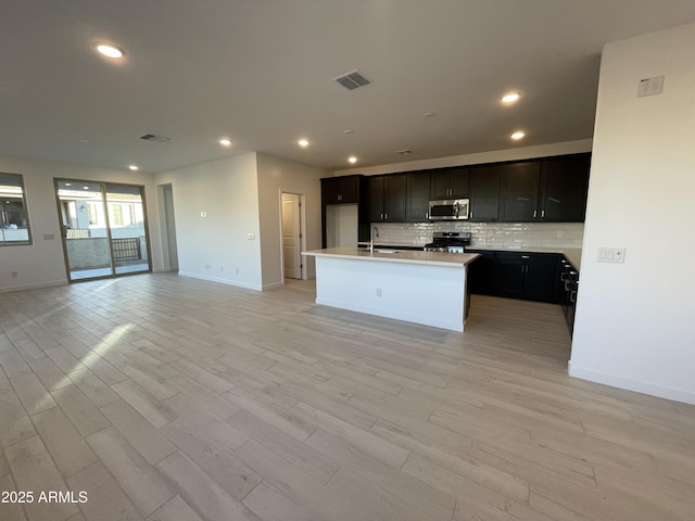 kitchen featuring visible vents, decorative backsplash, appliances with stainless steel finishes, open floor plan, and a sink