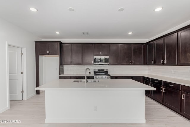 kitchen with a center island with sink, light countertops, appliances with stainless steel finishes, dark brown cabinetry, and a sink