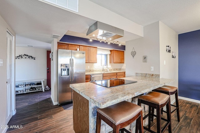 kitchen featuring kitchen peninsula, a textured ceiling, stainless steel appliances, a kitchen bar, and sink