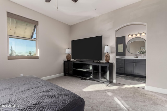 bedroom featuring light carpet, ensuite bathroom, ceiling fan, and sink