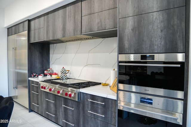 kitchen featuring light tile patterned floors, modern cabinets, appliances with stainless steel finishes, light stone counters, and backsplash