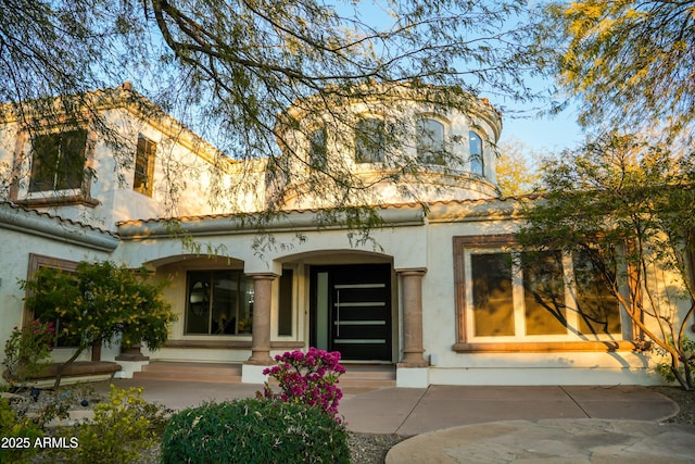 back of property with entry steps, a tiled roof, and stucco siding