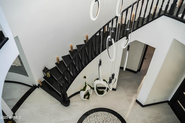 stairway featuring a towering ceiling, tile patterned flooring, and baseboards