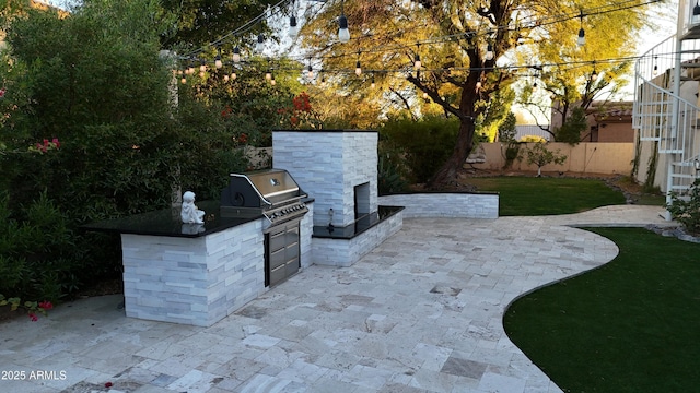 view of patio featuring grilling area, exterior fireplace, an outdoor kitchen, and a fenced backyard