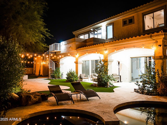 back of house at night featuring a balcony, a patio area, and stairway