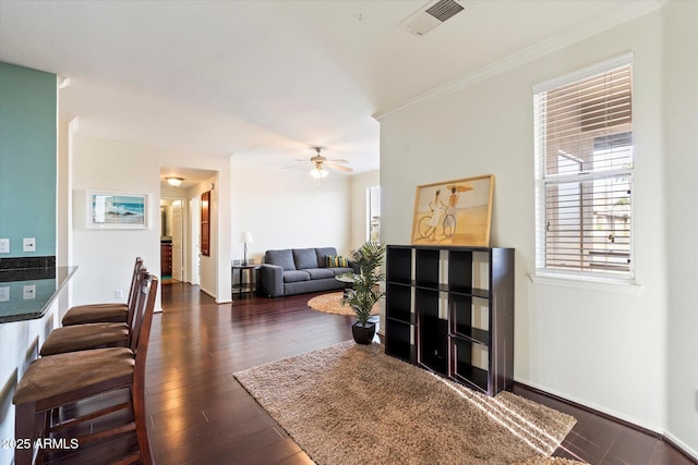 living area with baseboards, visible vents, dark wood finished floors, a ceiling fan, and ornamental molding