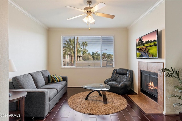 living room featuring dark wood-type flooring, ornamental molding, a tiled fireplace, and ceiling fan